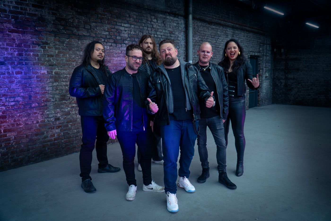 De band met duimen omhoog en een metal-hand voor een paars verlichte muur